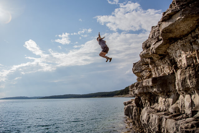 A man diving off a cliff and into an open body of water 