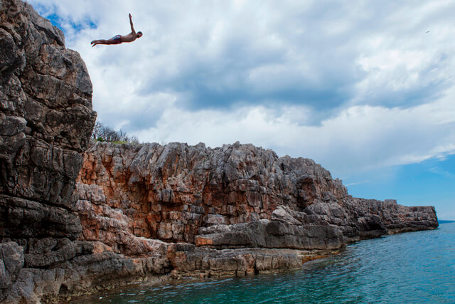 A man jumping from a height off a cliff and into the sea