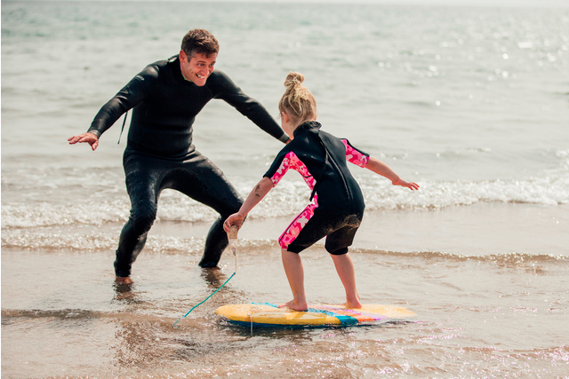 A man teaching a young girl how to surf on the shore
