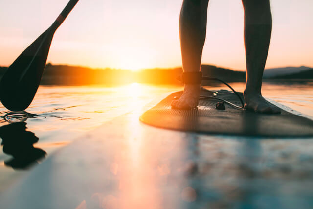 A person balancing on a paddleboard in the water at sunset