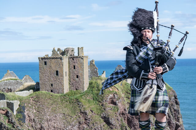 A Scottish bagpiper played stood alongside the ruins of Dunnottar Castle